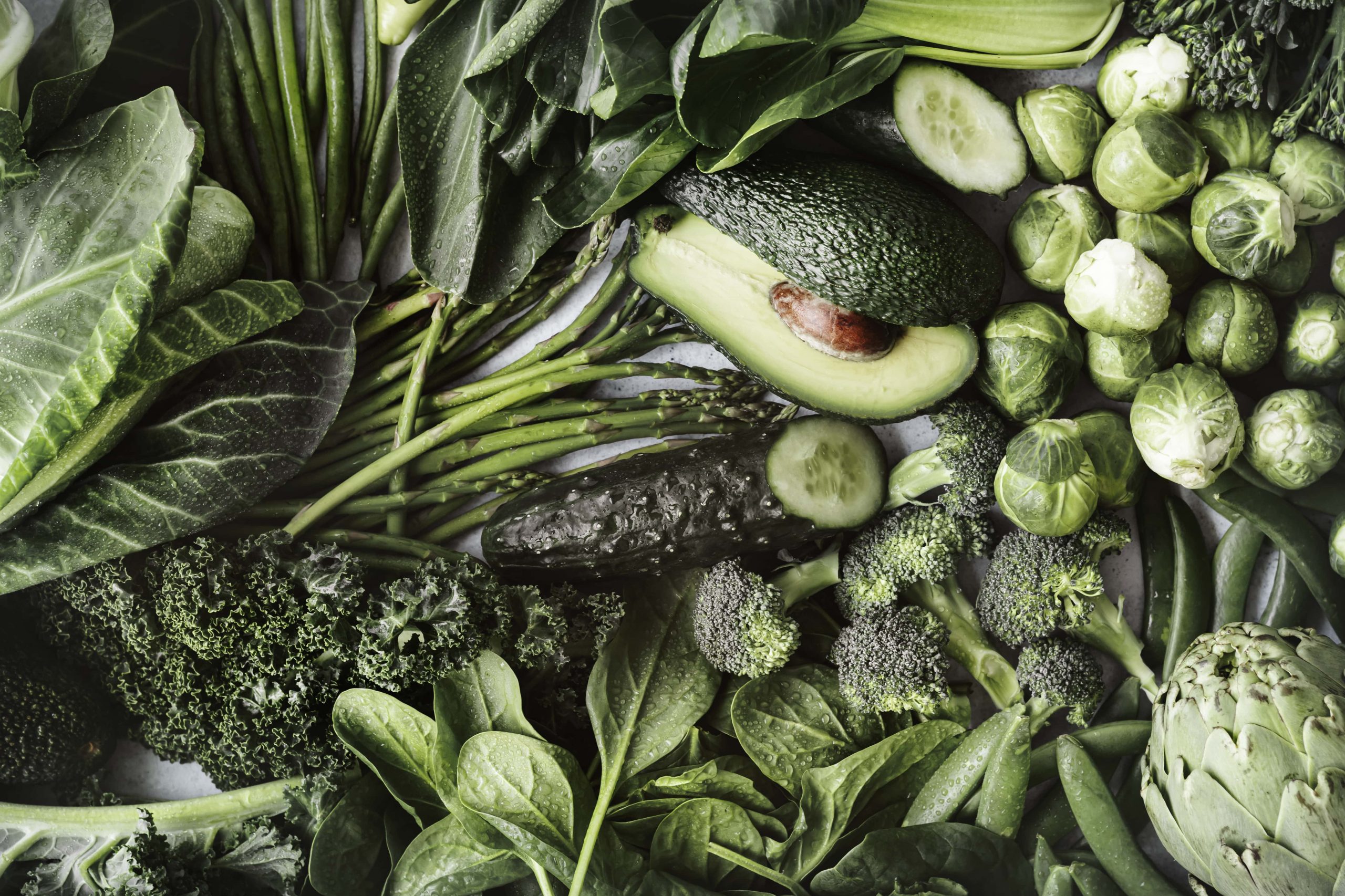 Avocado, broccoli and leafy greens arranged on a dark background