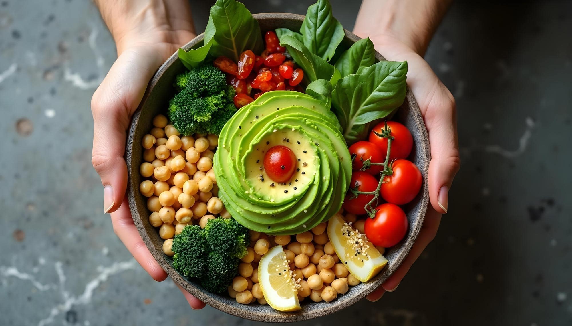 Hände halten eine pflanzliche Bowl mit Kichererbsen, Avocado und Gemüse