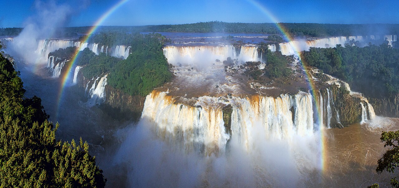Panorama der Iguazú-Wasserfälle mit Wald, Gischt und Regenbogen